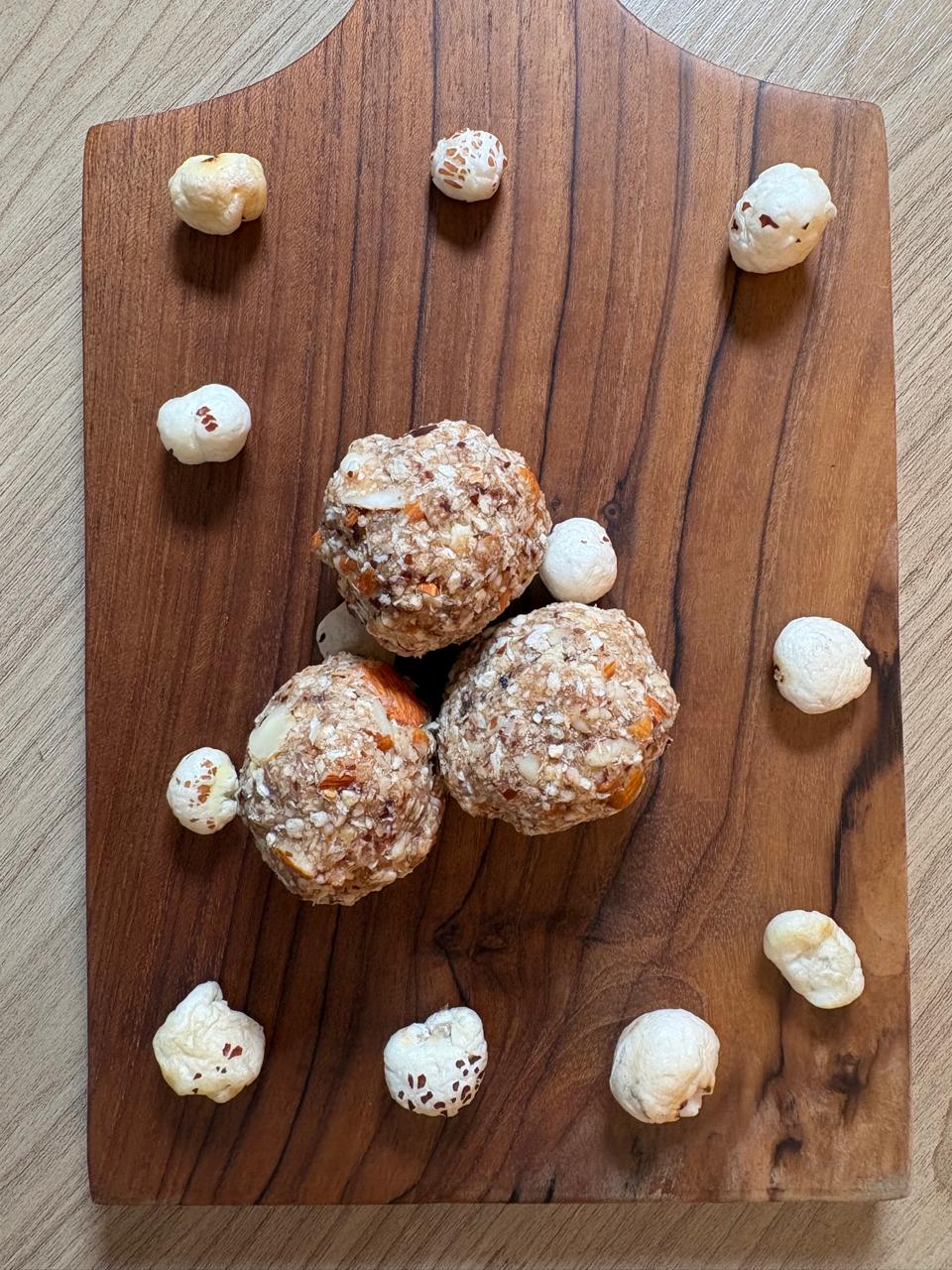Makhana ladoo with dates, almonds and coconut on a wooden board with puffed makhana
