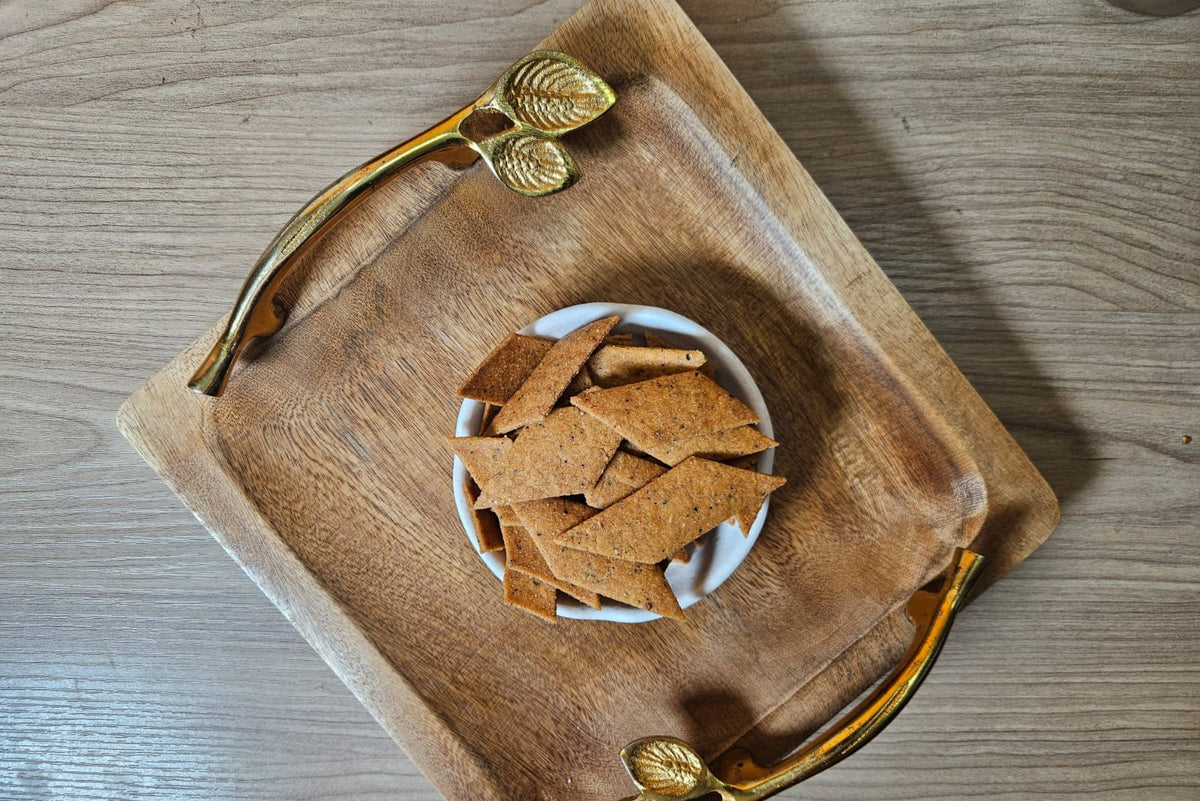 Whole wheat cheese crackers from Fluffiesta Gurgaon in a white bowl on a wooden serving tray with gold leaf handles, top view