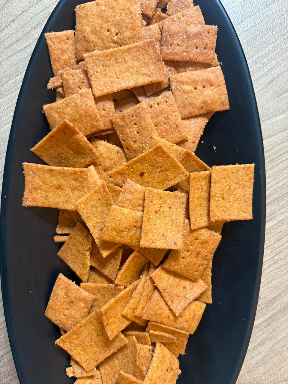 Peri peri whole wheat crackers arranged on a black plate on a wooden table, Fluffiesta Gurgaon