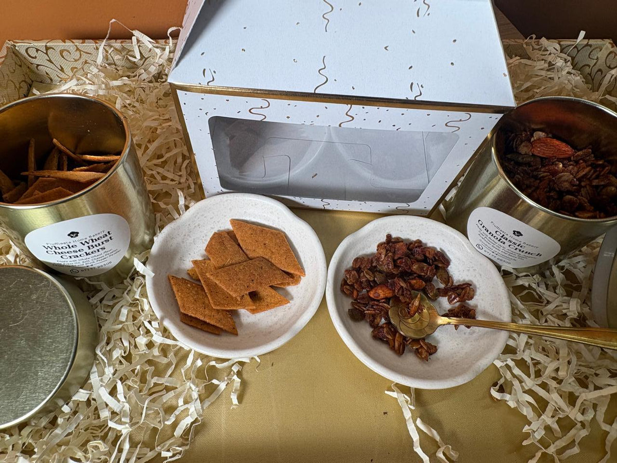 Diwali hamper spread: window gift box, gold tins and plates of crackers and granola on gold fabric