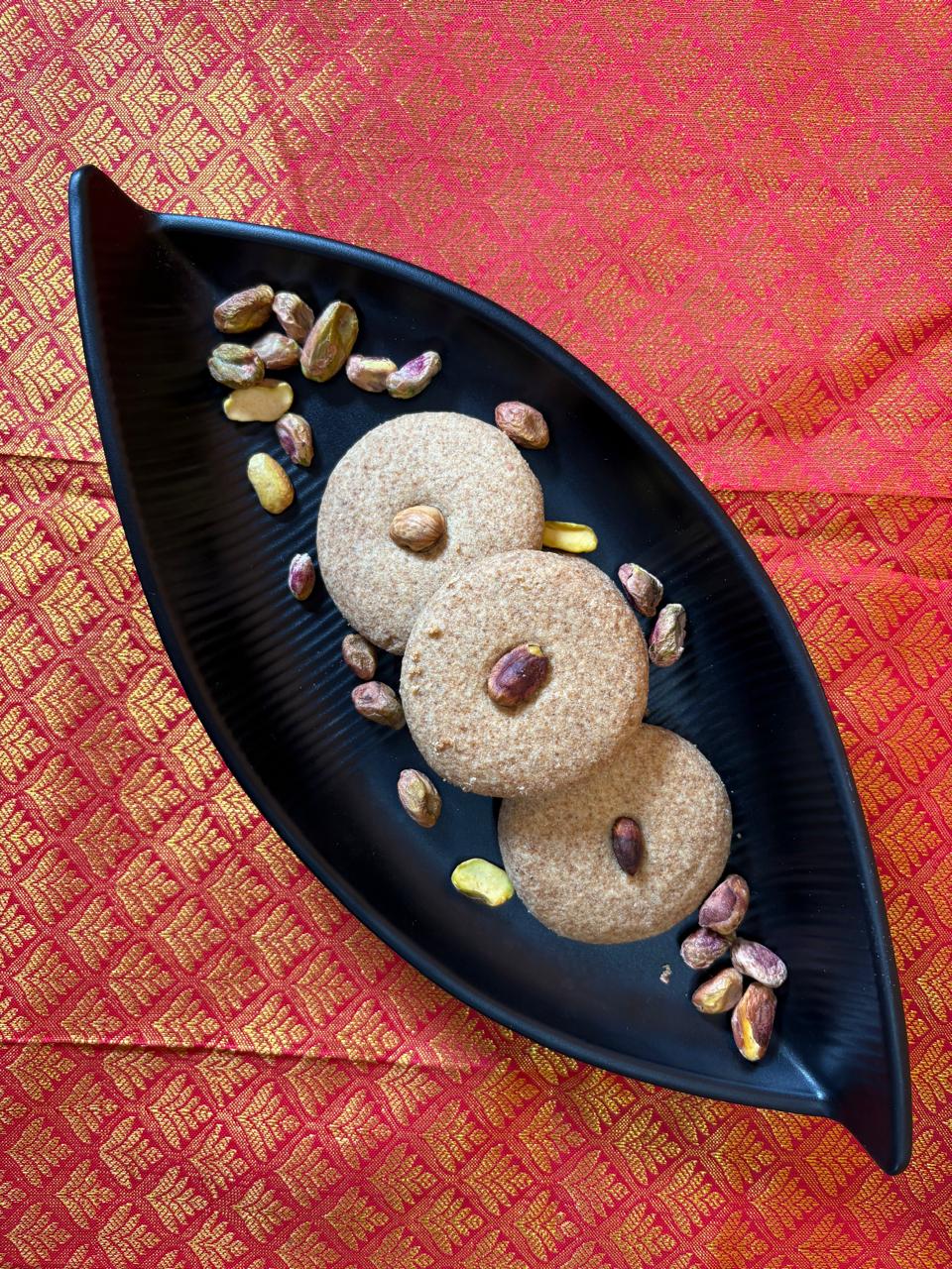 Jowar nankhatai topped with pistachio on a black serving tray with pistachios