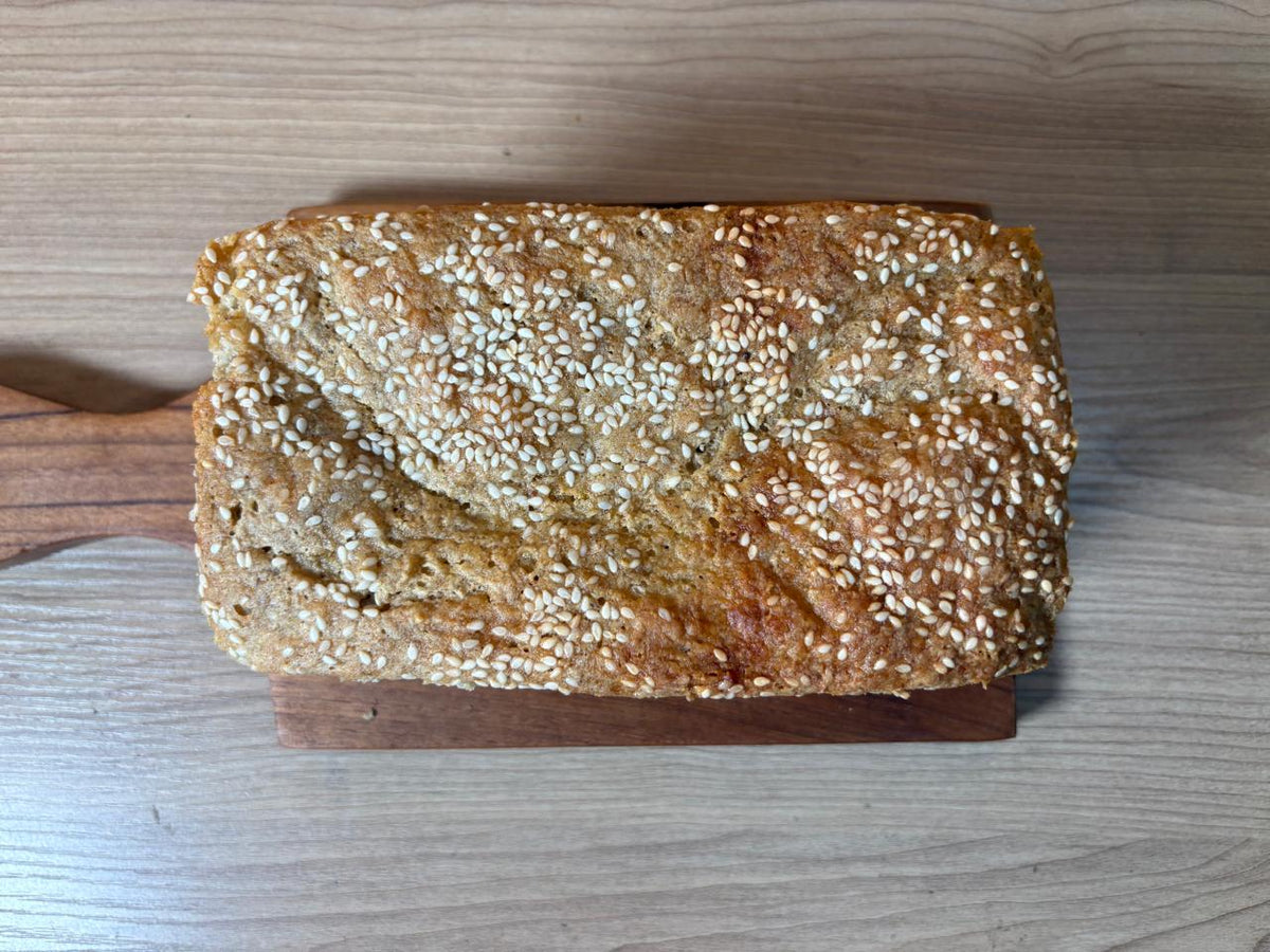 Whole jowar bread loaf topped with sesame seeds on a wooden board