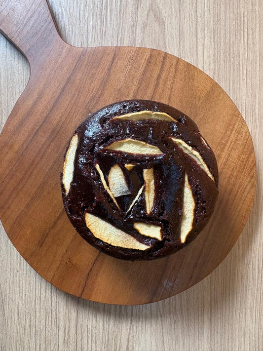 Dark chocolate apple cake topped with apple slices on a wooden board, Fluffiesta Gurgaon
