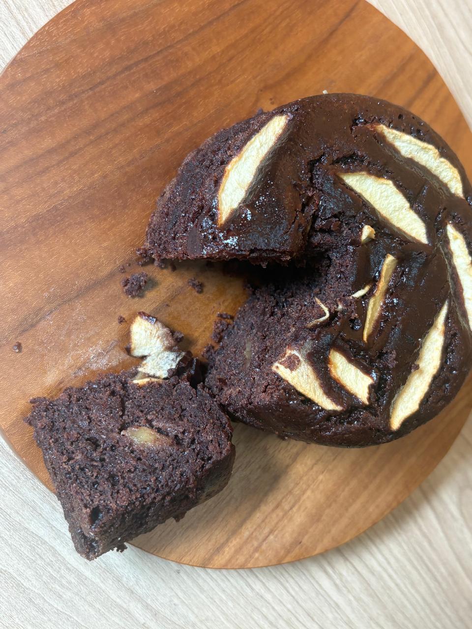 Dark chocolate apple cake with a slice cut out on a wooden board