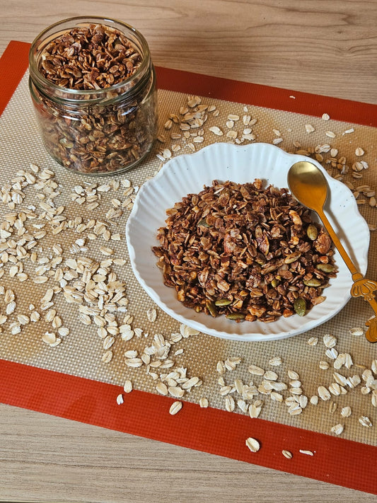 Granola in a glass jar and a white bowl with oats on a baking mat